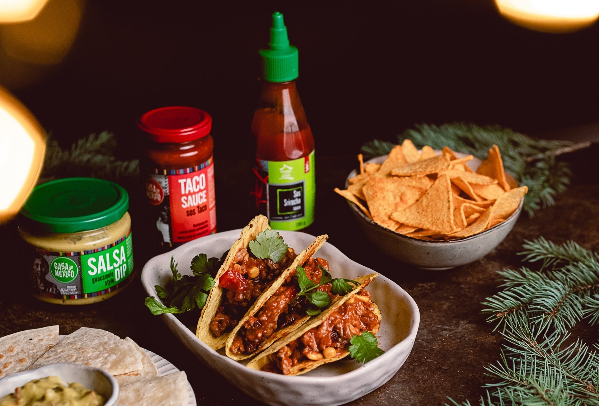 Trzy tacosy z chili con carne i kolendrą obok słoików sosu taco i salsy Casa del Sur