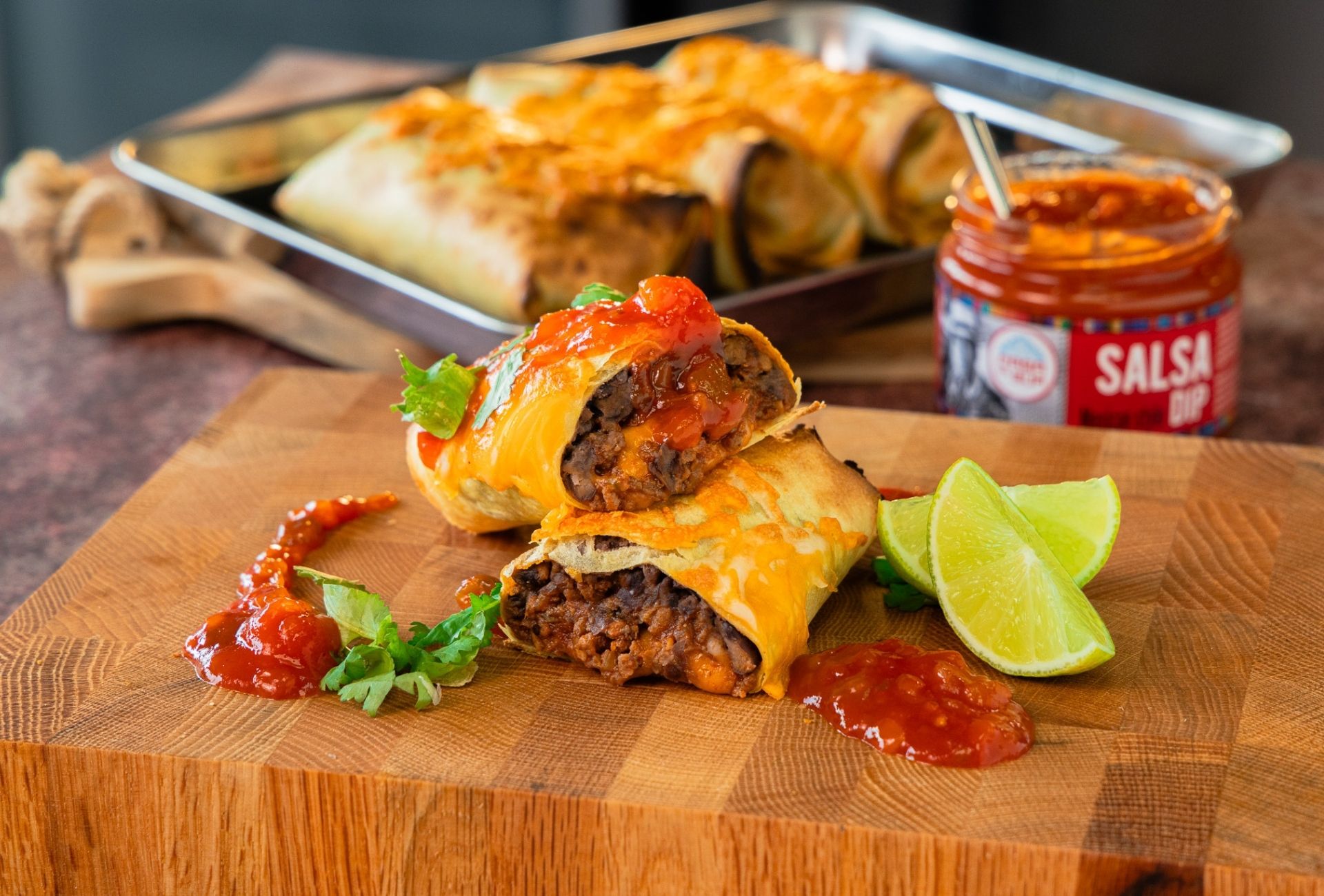 Zapiekana chimichanga z mięsem mielonym, serem i salsą pomidorową na drewnianej desce, podana z cząstkami limonki obok słoiczka Salsa Dip Casa del Sur.