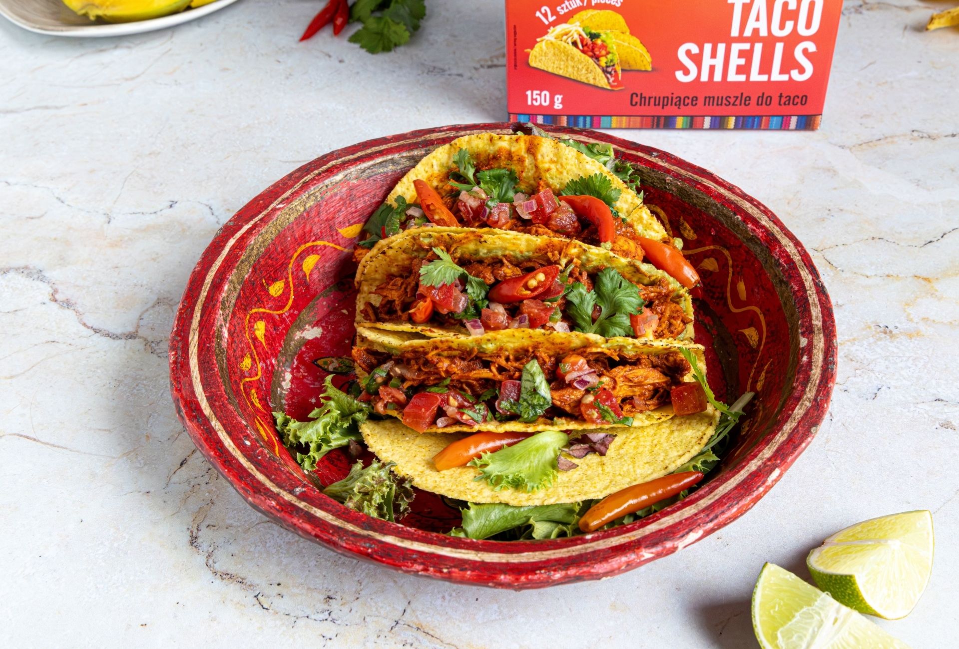 Tacos z szarpanym kurczakiem, salsą pomidorową i kolendrą podane w czerwonej misce, obok słoiczka papryczek Pepperoni Pepper marki Casa del Sur.